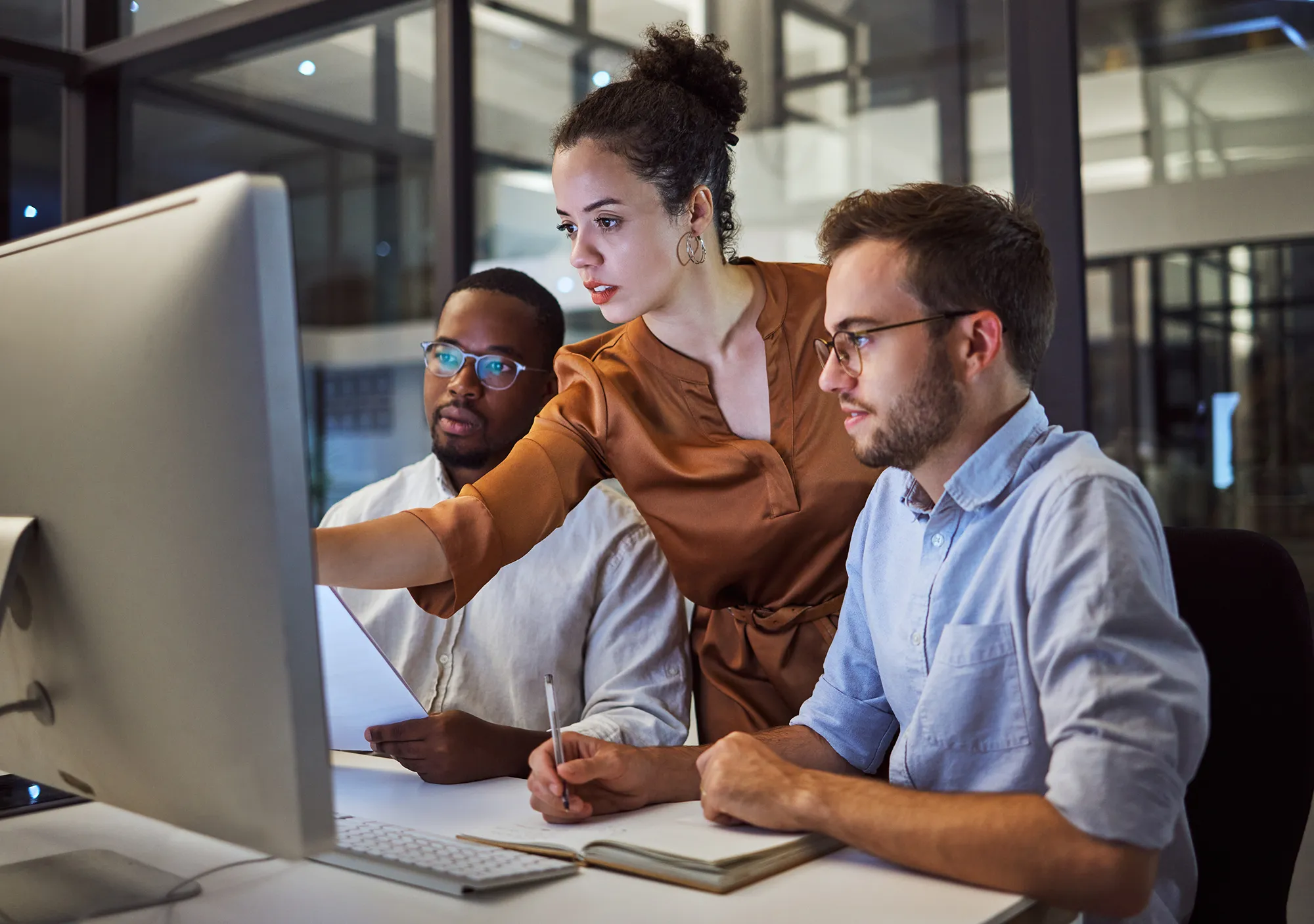 2 men and a woman looking at a computer screen solving a problem