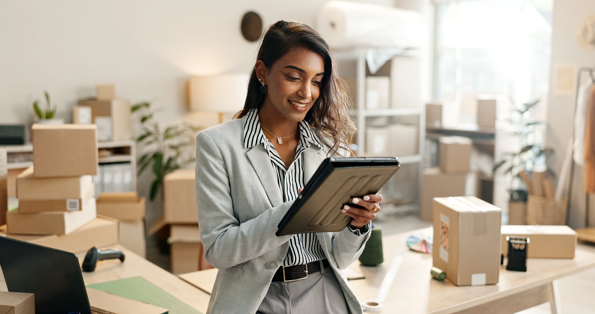 A woman on her tablet, with boxes and packaging behind her.